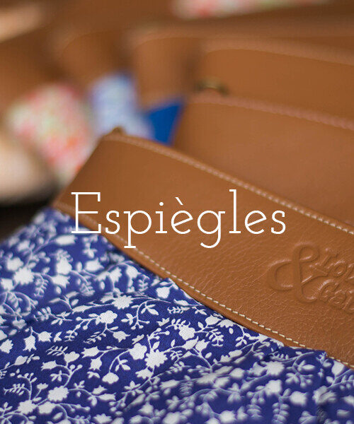 Espiègles – voir la collection. Pochette en tissu bleu fleuri barrée d’une bande de cuir camel